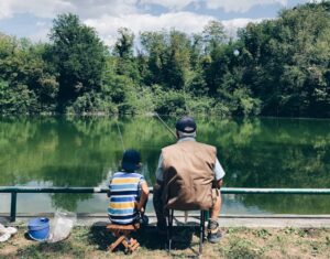 man in black shirt sitting on chair near lake during daytime